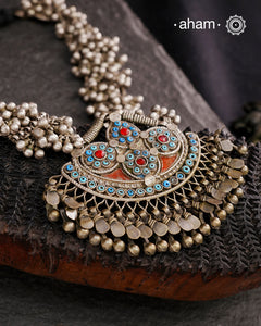 This Tribal Silver Neckpiece features a stunning pendant that was originally a headpiece complemented by tribal chains with multiple ghungroos for added drama. A true treasure for any jewellery lover.