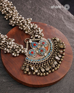 This Tribal Silver Neckpiece features a stunning pendant that was originally a headpiece complemented by tribal chains with multiple ghungroos for added drama. A true treasure for any jewellery lover.
