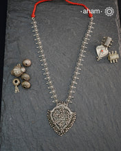This Tribal Silver Neckpiece features a heart-shaped pendant adorned with intricately crafted peacocks at the top, symbolizing grace and beauty. Multiple small ghungroos hang delicately from the pendant, adding subtle movement and traditional charm. The side bands are embellished with finely detailed floral motifs, enhancing the piece’s artisanal appeal. Crafted entirely in silver, this neckpiece combines cultural symbolism with expert craftsmanship, making it a distinctive accessory for those who appreciat