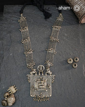 This expertly crafted silver neckpiece features a square amulet intricately depicting Lord Shiva alongside Nandi, embodying traditional tribal artistry. The side chains adorned with numerous ghungroos add a rhythmic charm, enhancing its cultural authenticity. Perfect for those who appreciate heritage craftsmanship and spiritual symbolism in their jewelry collection.