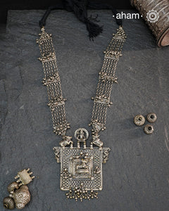 This expertly crafted silver neckpiece features a square amulet intricately depicting Lord Shiva alongside Nandi, embodying traditional tribal artistry. The side chains adorned with numerous ghungroos add a rhythmic charm, enhancing its cultural authenticity. Perfect for those who appreciate heritage craftsmanship and spiritual symbolism in their jewelry collection.
