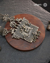 This expertly crafted silver neckpiece features a square amulet intricately depicting Lord Shiva alongside Nandi, embodying traditional tribal artistry. The side chains adorned with numerous ghungroos add a rhythmic charm, enhancing its cultural authenticity. Perfect for those who appreciate heritage craftsmanship and spiritual symbolism in their jewelry collection.