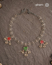 This expertly crafted Tribal Silver Neckpiece showcases intricate flower designs enhanced by glass drop highlights. Designed to complement traditional attire, it is an excellent choice for Navratri and other festive occasions.