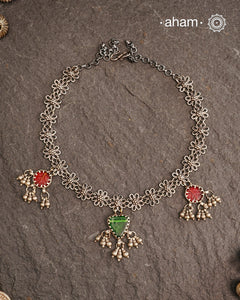 This expertly crafted Tribal Silver Neckpiece showcases intricate flower designs enhanced by glass drop highlights. Designed to complement traditional attire, it is an excellent choice for Navratri and other festive occasions.