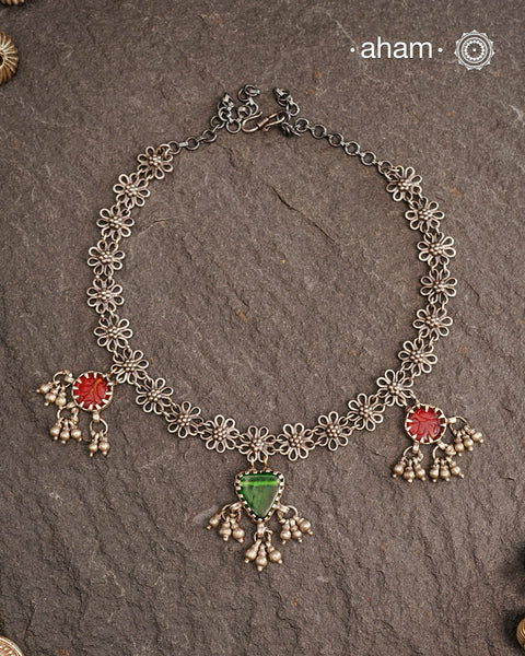 This expertly crafted Tribal Silver Neckpiece showcases intricate flower designs enhanced by glass drop highlights. Designed to complement traditional attire, it is an excellent choice for Navratri and other festive occasions.