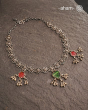 This expertly crafted Tribal Silver Neckpiece showcases intricate flower designs enhanced by glass drop highlights. Designed to complement traditional attire, it is an excellent choice for Navratri and other festive occasions.