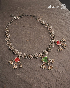 This expertly crafted Tribal Silver Neckpiece showcases intricate flower designs enhanced by glass drop highlights. Designed to complement traditional attire, it is an excellent choice for Navratri and other festive occasions.