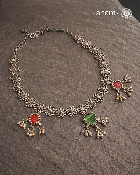 This expertly crafted Tribal Silver Neckpiece showcases intricate flower designs enhanced by glass drop highlights. Designed to complement traditional attire, it is an excellent choice for Navratri and other festive occasions.