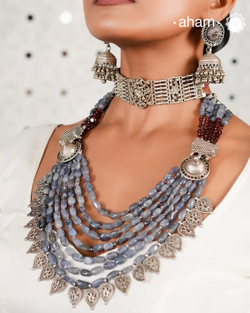 This Tribal Silver Neckpiece is a unique masterpiece designed to make a bold statement. Crafted from vintage silver pieces, it features tumbled iolite stones and a vibrant garnet accent at the top. Its versatile design complements both traditional and western outfits, offering a distinctive touch to your style. Perfect for those who appreciate unique statement pieces. 