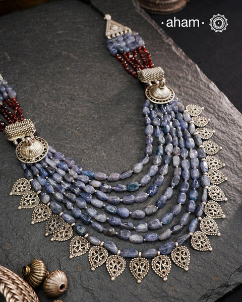 This Tribal Silver Neckpiece is a unique masterpiece designed to make a bold statement. Crafted from vintage silver pieces, it features tumbled iolite stones and a vibrant garnet accent at the top. Its versatile design complements both traditional and western outfits, offering a distinctive touch to your style. Perfect for those who appreciate unique statement pieces.
