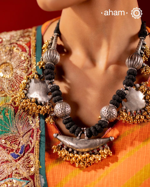 Elevate your style with this Tribal Two Tone Silver Neckpiece, featuring a captivating amulet center framed by elegant paan-shaped beads. The gold-dipped ghungroos add a stunning dual-tone contrast, making this piece truly one-of-a-kind. Perfect for those who want to make a bold cultural statement while embracing exquisite craftsmanship. Don’t miss the chance to own a unique accessory.