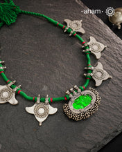 This Tribal Silver Neckpiece showcases a vibrant green glass pendant at its center, enhanced by meticulously hand-tied tiny ghungroos. On each side, three finely crafted silver leaves create a harmonious and elegant design. Ideal for layering during Navratri, this piece blends traditional artistry with festive sophistication to complement your celebration attire.