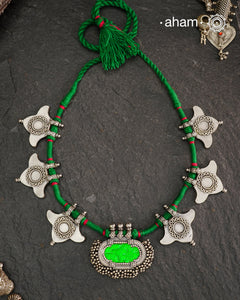 This Tribal Silver Neckpiece showcases a vibrant green glass pendant at its center, enhanced by meticulously hand-tied tiny ghungroos. On each side, three finely crafted silver leaves create a harmonious and elegant design. Ideal for layering during Navratri, this piece blends traditional artistry with festive sophistication to complement your celebration attire.