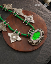 This Tribal Silver Neckpiece showcases a vibrant green glass pendant at its center, enhanced by meticulously hand-tied tiny ghungroos. On each side, three finely crafted silver leaves create a harmonious and elegant design. Ideal for layering during Navratri, this piece blends traditional artistry with festive sophistication to complement your celebration attire.