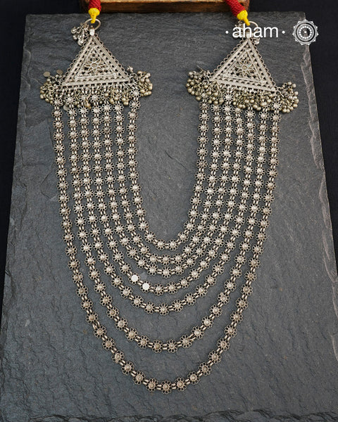 This Tribal Multi Line Silver Neckpiece is a magnificent classic Rani haar featuring seven intricately crafted lines, known as Satlada. It is adorned with a delicate floral pattern and accented by two prominent triangular motifs at each end. This vintage design exudes timeless elegance and cultural richness, making it a treasured heirloom piece meant to be passed down through generations. A neckpiece truly fit for a queen.