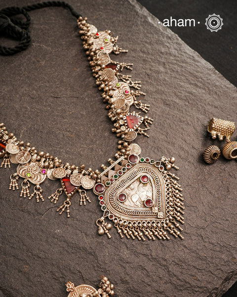 This Tribal Silver Neckpiece features a stunning pendant as the central piece and multiple small amulets and glass beads along with multiple ghungroos for added drama. A true treasure for any jewellery lover.