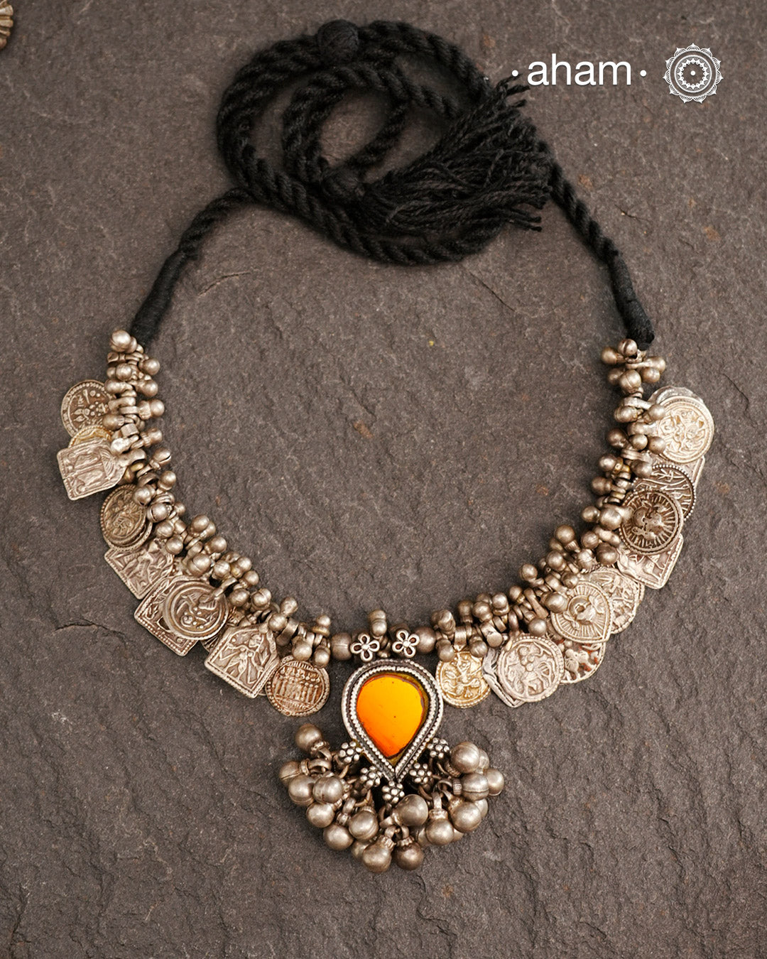 This Tribal Silver Neckpiece features a stunning glass pendant as the central piece and multiple small amulets and glass beads along with multiple ghungroos for added drama. A true treasure for any jewellery lover.
