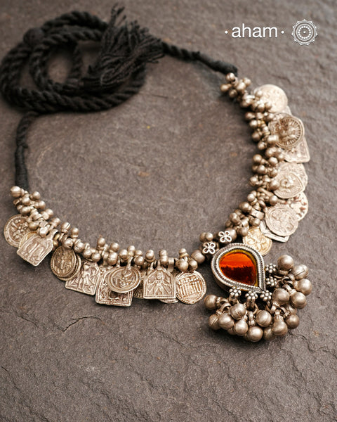 This Tribal Silver Neckpiece features a stunning glass pendant as the central piece and multiple small amulets and glass beads along with multiple ghungroos for added drama. A true treasure for any jewellery lover.