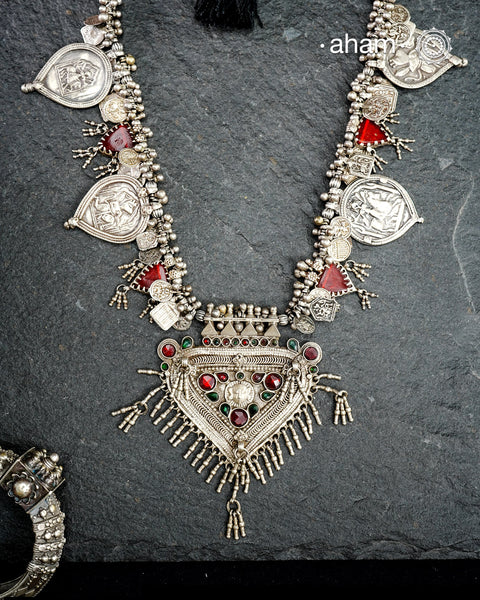 This Tribal Silver Neckpiece features a stunning pendant as the central piece and multiple small amulets and glass beads along with multiple ghungroos for added drama. A true treasure for any jewellery lover.