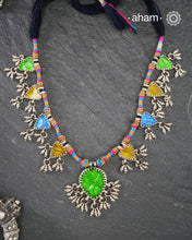 This Tribal Silver Neckpiece showcases a vibrant green glass pendant at its center, enhanced by meticulously hand-tied tiny ghungroos. On each side, three finely crafted silver leaves create a harmonious and elegant design. Ideal for layering during Navratri, this piece blends traditional artistry with festive sophistication to complement your celebration attire.
