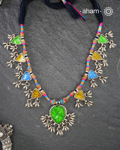This Tribal Silver Neckpiece showcases a vibrant green glass pendant at its center, enhanced by meticulously hand-tied tiny ghungroos. On each side, three finely crafted silver leaves create a harmonious and elegant design. Ideal for layering during Navratri, this piece blends traditional artistry with festive sophistication to complement your celebration attire.