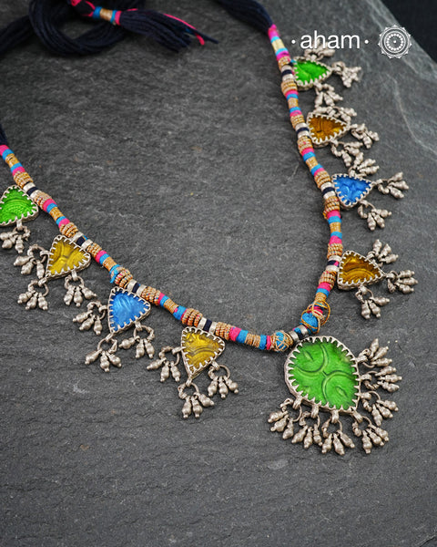 This Tribal Silver Neckpiece showcases a vibrant green glass pendant at its center, enhanced by meticulously hand-tied tiny ghungroos. On each side, three finely crafted silver leaves create a harmonious and elegant design. Ideal for layering during Navratri, this piece blends traditional artistry with festive sophistication to complement your celebration attire.