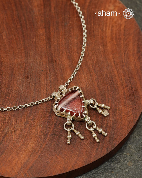 A charming piece inspired by traditional tribal adornments, this neckpiece features a muddy red glass pendant accented with silver ghungroos that sway gently with movement. The striking colour of the glass contrasts beautifully with the rustic silver finish, creating a look that is both distinctive and effortless.

Lightweight and easy to style, it pairs beautifully with handloom sarees, cotton kurtas, dresses, and everyday separates. Its understated size and playful detailing make it perfect for those who 