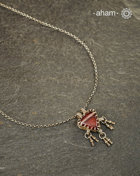 A charming piece inspired by traditional tribal adornments, this neckpiece features a muddy red glass pendant accented with silver ghungroos that sway gently with movement. The striking colour of the glass contrasts beautifully with the rustic silver finish, creating a look that is both distinctive and effortless.

Lightweight and easy to style, it pairs beautifully with handloom sarees, cotton kurtas, dresses, and everyday separates. Its understated size and playful detailing make it perfect for those who 