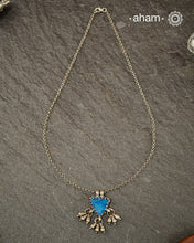 A charming piece inspired by traditional tribal adornments, this neckpiece features a vibrant blue glass pendant accented with silver ghungroos that sway gently with movement. The striking colour of the glass contrasts beautifully with the rustic silver finish, creating a look that is both distinctive and effortless.

Lightweight and easy to style, it pairs beautifully with handloom sarees, cotton kurtas, dresses, and everyday separates. Its understated size and playful detailing make it perfect for those w