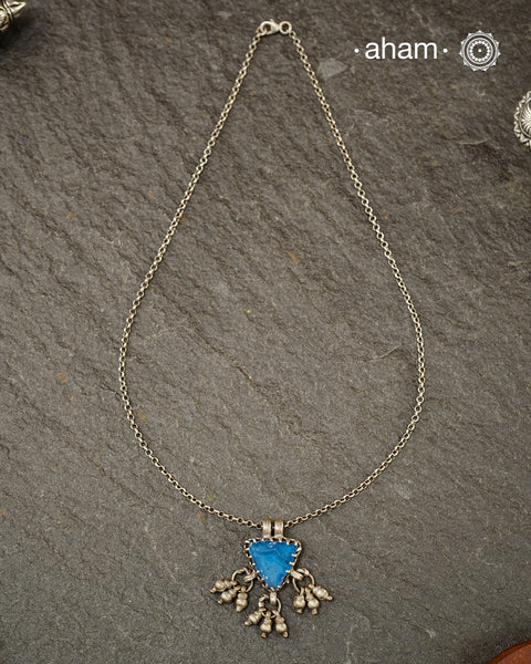 A charming piece inspired by traditional tribal adornments, this neckpiece features a vibrant blue glass pendant accented with silver ghungroos that sway gently with movement. The striking colour of the glass contrasts beautifully with the rustic silver finish, creating a look that is both distinctive and effortless.

Lightweight and easy to style, it pairs beautifully with handloom sarees, cotton kurtas, dresses, and everyday separates. Its understated size and playful detailing make it perfect for those w