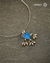 A charming piece inspired by traditional tribal adornments, this neckpiece features a vibrant blue glass pendant accented with silver ghungroos that sway gently with movement. The striking colour of the glass contrasts beautifully with the rustic silver finish, creating a look that is both distinctive and effortless.

Lightweight and easy to style, it pairs beautifully with handloom sarees, cotton kurtas, dresses, and everyday separates. Its understated size and playful detailing make it perfect for those w