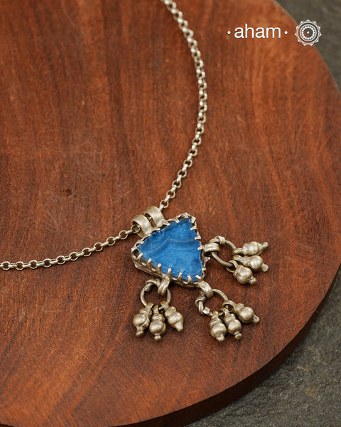 A charming piece inspired by traditional tribal adornments, this neckpiece features a vibrant blue glass pendant accented with silver ghungroos that sway gently with movement. The striking colour of the glass contrasts beautifully with the rustic silver finish, creating a look that is both distinctive and effortless.

Lightweight and easy to style, it pairs beautifully with handloom sarees, cotton kurtas, dresses, and everyday separates. Its understated size and playful detailing make it perfect for those w