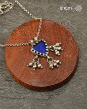 A charming piece inspired by traditional tribal adornments, this neckpiece features a vibrant blue glass pendant accented with silver ghungroos that sway gently with movement. The striking colour of the glass contrasts beautifully with the rustic silver finish, creating a look that is both distinctive and effortless.

Lightweight and easy to style, it pairs beautifully with handloom sarees, cotton kurtas, dresses, and everyday separates.