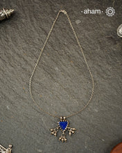 A charming piece inspired by traditional tribal adornments, this neckpiece features a vibrant blue glass pendant accented with silver ghungroos that sway gently with movement. The striking colour of the glass contrasts beautifully with the rustic silver finish, creating a look that is both distinctive and effortless.

Lightweight and easy to style, it pairs beautifully with handloom sarees, cotton kurtas, dresses, and everyday separates.
