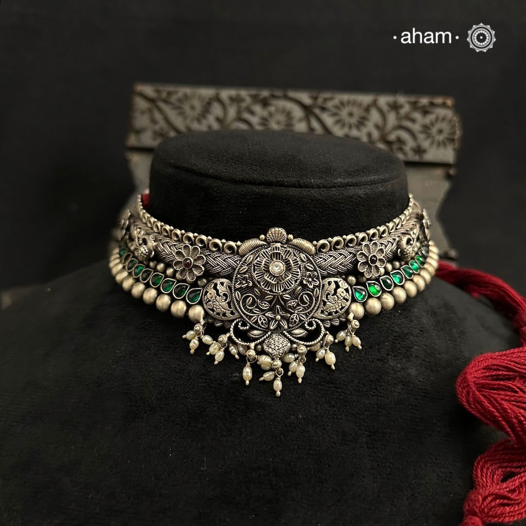 This Shivneri Silver Maharashtrian Thushi showcases the intricate craftsmanship of kolhapuri artisans Made from 92.5 silver, it features beautiful green stone highlights and elegant pearls for a stunning addition to any outfit. Expertly crafted, this necklace is perfect for those looking for a touch of traditional elegance.