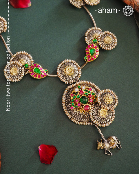 Handcrafted with love this noori dual tone neckpiece is a meticulous mix of royalty and artistry. Shine brighter adorned in this master piece with cultured pearls embellished around silver floral studs with gold polish, paisley  Peacock motifs with deep pink and green spinel, and Kamadhenu (an auspicious sacred cow in the Hindu mythology) motif in the center. Each piece is one of a kind, modern heirloom neckpiece that can be passed on from generations to generations.