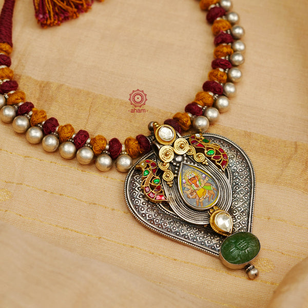 This Handpainted Ganesha Two Tone Silver Neckpiece features a beautifully crafted miniature hand painted ganesha with gold kundan highlights and two elegant peacocks. Handmade with intricate details, this neckpiece is a perfect accessory for any outfit and showcases a blend of traditional and contemporary design.