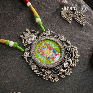 This hand-painted Shreenathji neckpiece is a true piece of art. The miniature Shreenathji is carefully painted by master artisans, set in silver with kundan work and strung on a comfortable cotton thread. Add a touch of culture and beauty to your outfit with this unique silver neckpiece.
