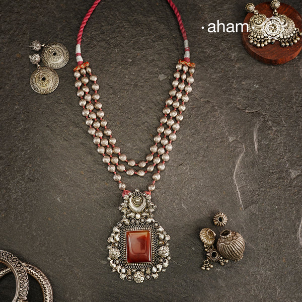 Exquisitely crafted Ira Silver Neckpiece featuring three elegant beaded lines that converge on a stunning pendant. The centerpiece showcases a rich carnelian coloured stone, meticulously surrounded by delicate pearl work, creating a harmonious balance of color and texture. This sophisticated design designed in 92.5 silver offers timeless appeal with a contemporary sensibility.