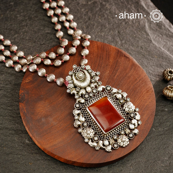 Exquisitely crafted Ira Silver Neckpiece featuring three elegant beaded lines that converge on a stunning pendant. The centerpiece showcases a rich carnelian coloured stone, meticulously surrounded by delicate pearl work, creating a harmonious balance of color and texture. This sophisticated design designed in 92.5 silver offers timeless appeal with a contemporary sensibility.