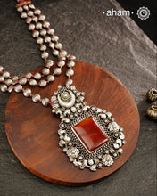 Exquisitely crafted Ira Silver Neckpiece featuring three elegant beaded lines that converge on a stunning pendant. The centerpiece showcases a rich carnelian coloured stone, meticulously surrounded by delicate pearl work, creating a harmonious balance of color and texture. This sophisticated design designed in 92.5 silver offers timeless appeal with a contemporary sensibility.