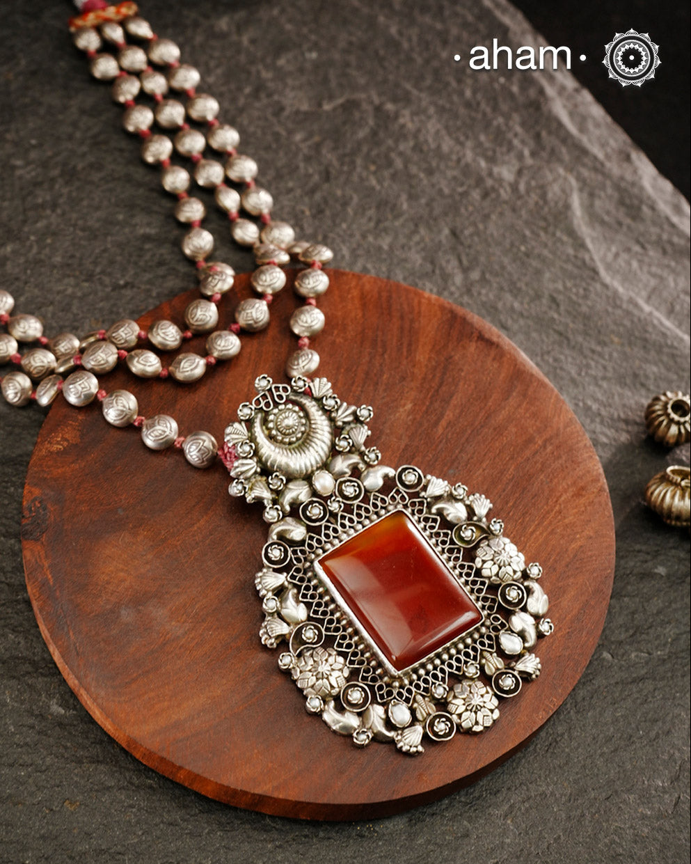 Exquisitely crafted Ira Silver Neckpiece featuring three elegant beaded lines that converge on a stunning pendant. The centerpiece showcases a rich carnelian coloured stone, meticulously surrounded by delicate pearl work, creating a harmonious balance of color and texture. This sophisticated design designed in 92.5 silver offers timeless appeal with a contemporary sensibility.
