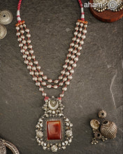 Exquisitely crafted Ira Silver Neckpiece featuring three elegant beaded lines that converge on a stunning pendant. The centerpiece showcases a rich carnelian coloured stone, meticulously surrounded by delicate pearl work, creating a harmonious balance of color and texture. This sophisticated design designed in 92.5 silver offers timeless appeal with a contemporary sensibility.