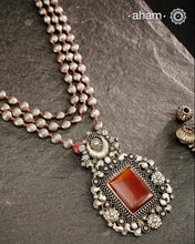 Exquisitely crafted Ira Silver Neckpiece featuring three elegant beaded lines that converge on a stunning pendant. The centerpiece showcases a rich carnelian coloured stone, meticulously surrounded by delicate pearl work, creating a harmonious balance of color and texture. This sophisticated design designed in 92.5 silver offers timeless appeal with a contemporary sensibility.