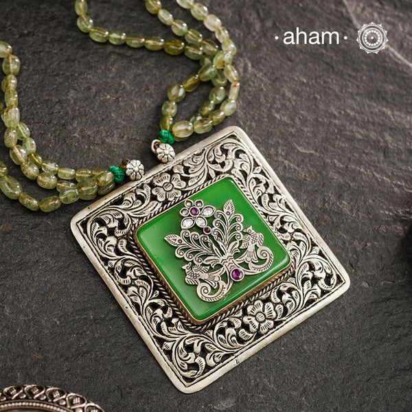 The Ira Silver Neckpiece features masterful chitai work with precise silver cutwork that sits on a luminous green center stone. The pendant is complemented by a strand of carefully selected semi-precious stone beads, enhancing its visual complexity. This exceptional piece demonstrates superior silversmithing techniques while offering a sophisticated aesthetic that transitions effortlessly from traditional to contemporary settings.