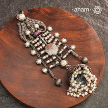 This unique Ganesha Pendant is a statement piece crafted in 92.5 silver. The intricate design features Ganesha at the top, flanked by delicately crafted peacocks on either side. A jhumka hangs at the bottom, adorned with pearl highlights for a touch of elegance. Elevate any outfit with this one-of-a-kind pendant.