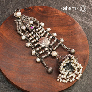 This unique Ganesha Pendant is a statement piece crafted in 92.5 silver. The intricate design features Ganesha at the top, flanked by delicately crafted peacocks on either side. A jhumka hangs at the bottom, adorned with pearl highlights for a touch of elegance. Elevate any outfit with this one-of-a-kind pendant.