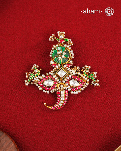 An intricately crafted statement pendant inspired by traditional artistry and symbolism. Featuring delicate peacock motifs on either side and tiger nail motif at the bottom, this striking design is adorned with vibrant deep pink and green kundan work, highlighted with luminous stone settings and intricate pearl detailing. At the centre sits a beautifully carved green stone, adding depth and character to the composition. Crafted in 92.5 silver with a rich gold polish finish, this pendant is designed to stand