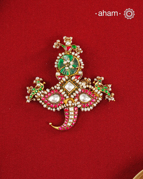 An intricately crafted statement pendant inspired by traditional artistry and symbolism. Featuring delicate peacock motifs on either side and tiger nail motif at the bottom, this striking design is adorned with vibrant deep pink and green kundan work, highlighted with luminous stone settings and intricate pearl detailing. At the centre sits a beautifully carved green stone, adding depth and character to the composition. Crafted in 92.5 silver with a rich gold polish finish, this pendant is designed to stand