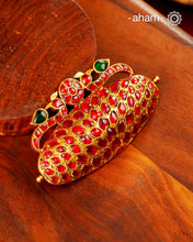 Inspired by the grandeur of traditional South Indian jewellery, this statement pendant is handcrafted in 92.5 sterling silver and finished with a rich gold polish. The design is crowned by a pair of graceful peacocks, a timeless symbol of beauty, prosperity, and auspiciousness, framing a central kundan motif.

The sculptural form is entirely adorned with hand-set ruby-toned kundan stones, creating a striking play of colour and craftsmanship. 